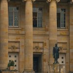 Fachada de um edifício público com colunas e estátua na entrada.