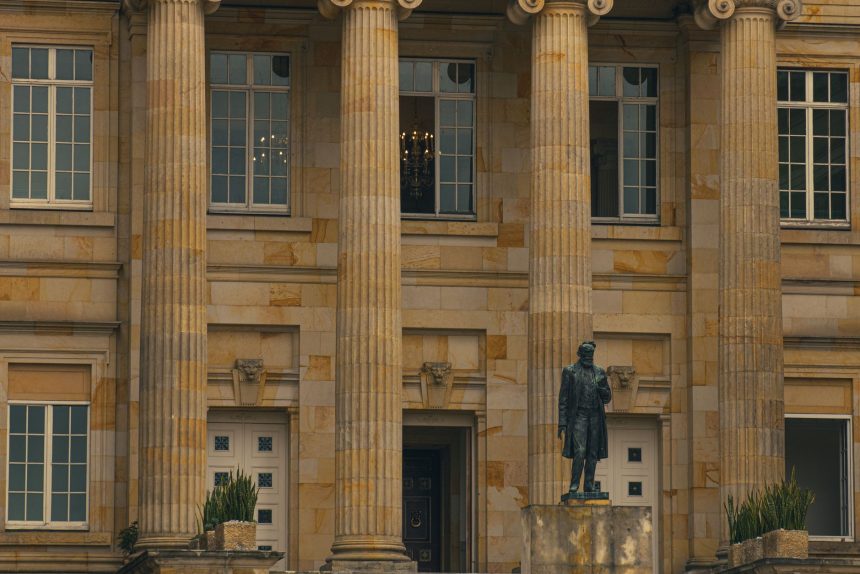 Fachada de um edifício público com colunas e estátua na entrada.