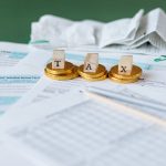Close de formulários financeiros, recibos e moedas sobre uma superfície, representando contabilidade e pagamentos.