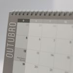 Close de um calendário de mesa aberto no mês de outubro, com encadernação espiral.