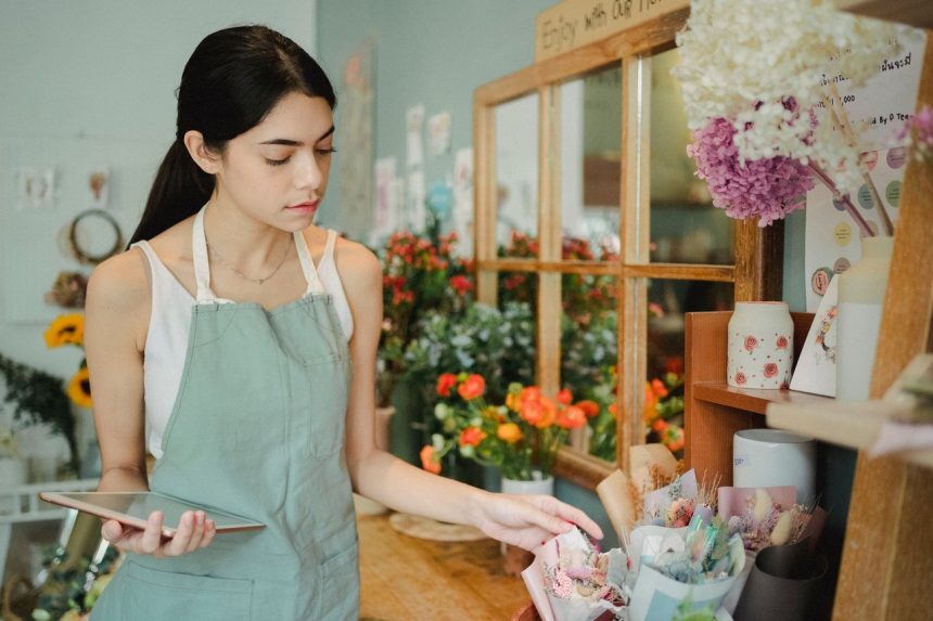 Floricultora consulta um tablet enquanto trabalha em sua loja de flores.