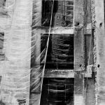 Fachada de um edifício coberta por uma tela de proteção durante uma obra, em imagem em preto e branco.