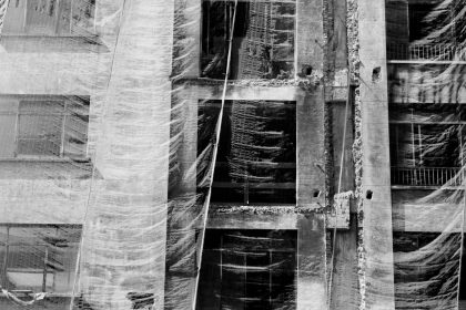 Fachada de um edifício coberta por uma tela de proteção durante uma obra, em imagem em preto e branco.