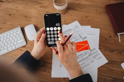 Mãos usando a calculadora de um smartphone sobre documentos financeiros.