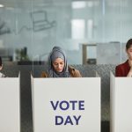 Três mulheres votam em cabines individuais durante uma eleição.