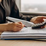 Pessoa usa uma calculadora enquanto analisa documentos financeiros sobre uma mesa de escritório.