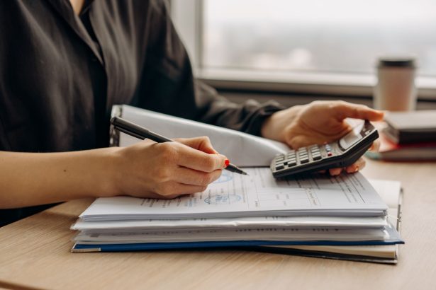 Pessoa usa uma calculadora enquanto analisa documentos financeiros sobre uma mesa de escritório.