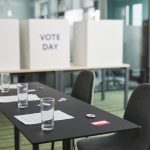 Seção eleitoral preparada, com mesas, cadeiras e cabines de votação em uma sala.