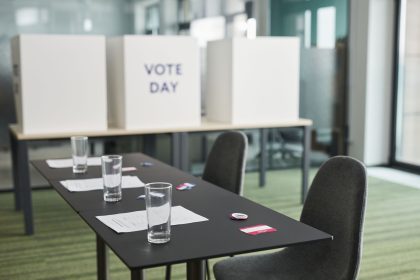 Seção eleitoral preparada, com mesas, cadeiras e cabines de votação em uma sala.