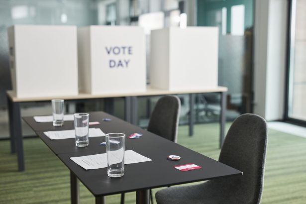 Seção eleitoral preparada, com mesas, cadeiras e cabines de votação em uma sala.